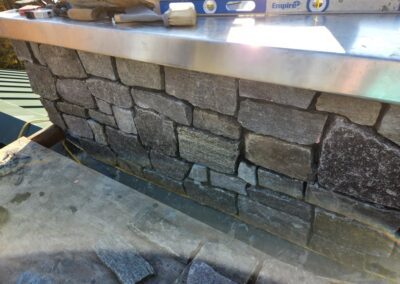 Stone masonry wall under construction with irregularly shaped stones, metal level tool, and brush on top, showcasing craftsmanship in property management and outdoor stonework.