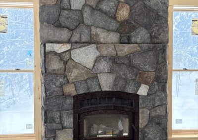 Rustic stone fireplace with large irregular grey and brown stones, set between two windows in a room under construction, showcasing Excelsior Property Management's focus on quality home features and property updates.