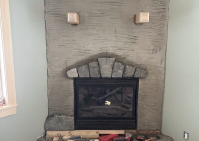 Fireplace under construction with stonework and cement base in a room with light green walls and wooden ceiling, featuring tools and materials for home renovation and property management.